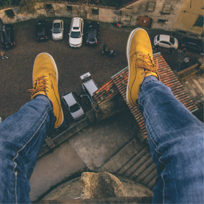 Someone sitting very high up on a building and looking down at their yellow sneakers